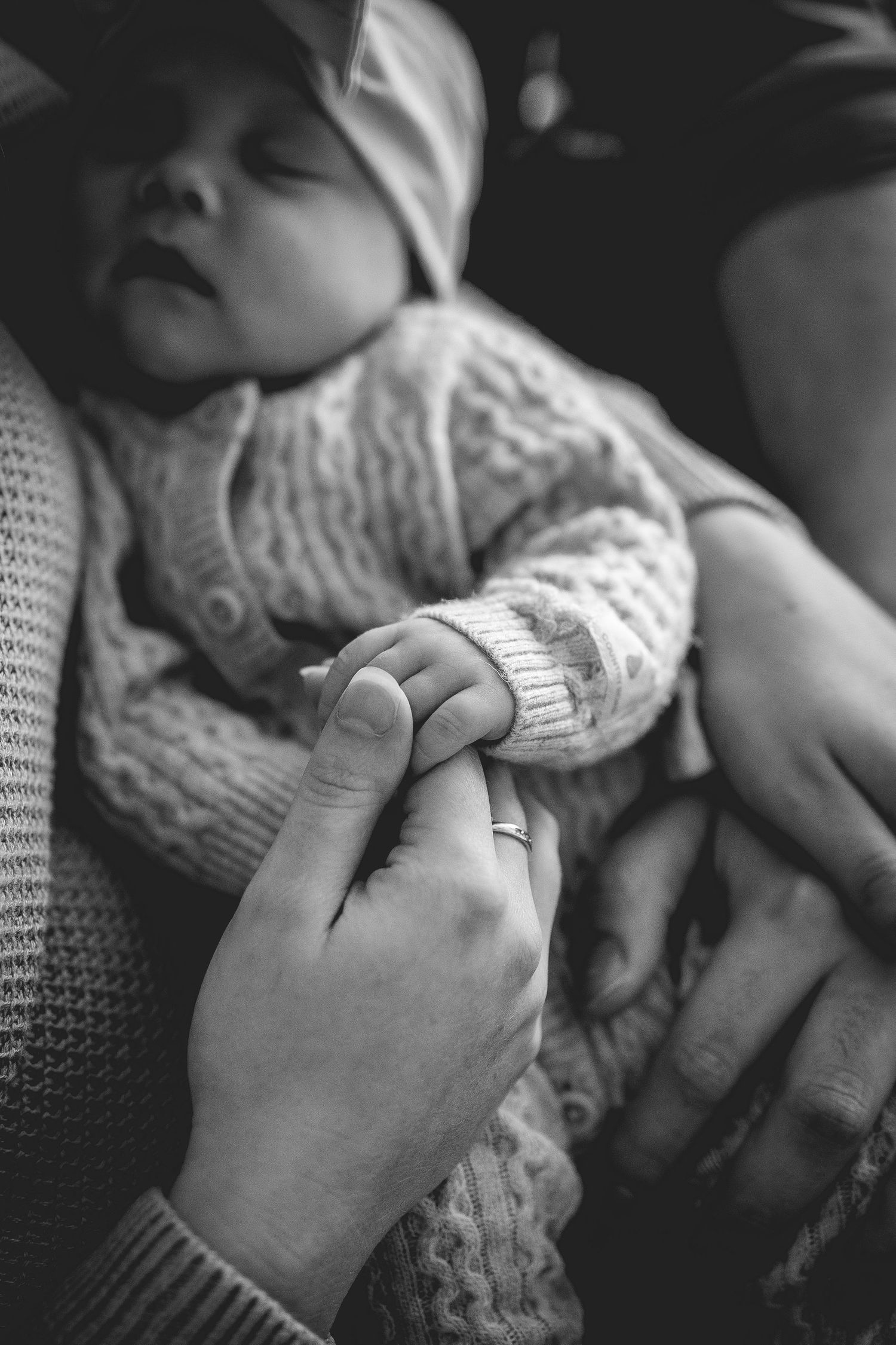 Close up of tiny hand grasping adult finger while wearing white knit sweater.