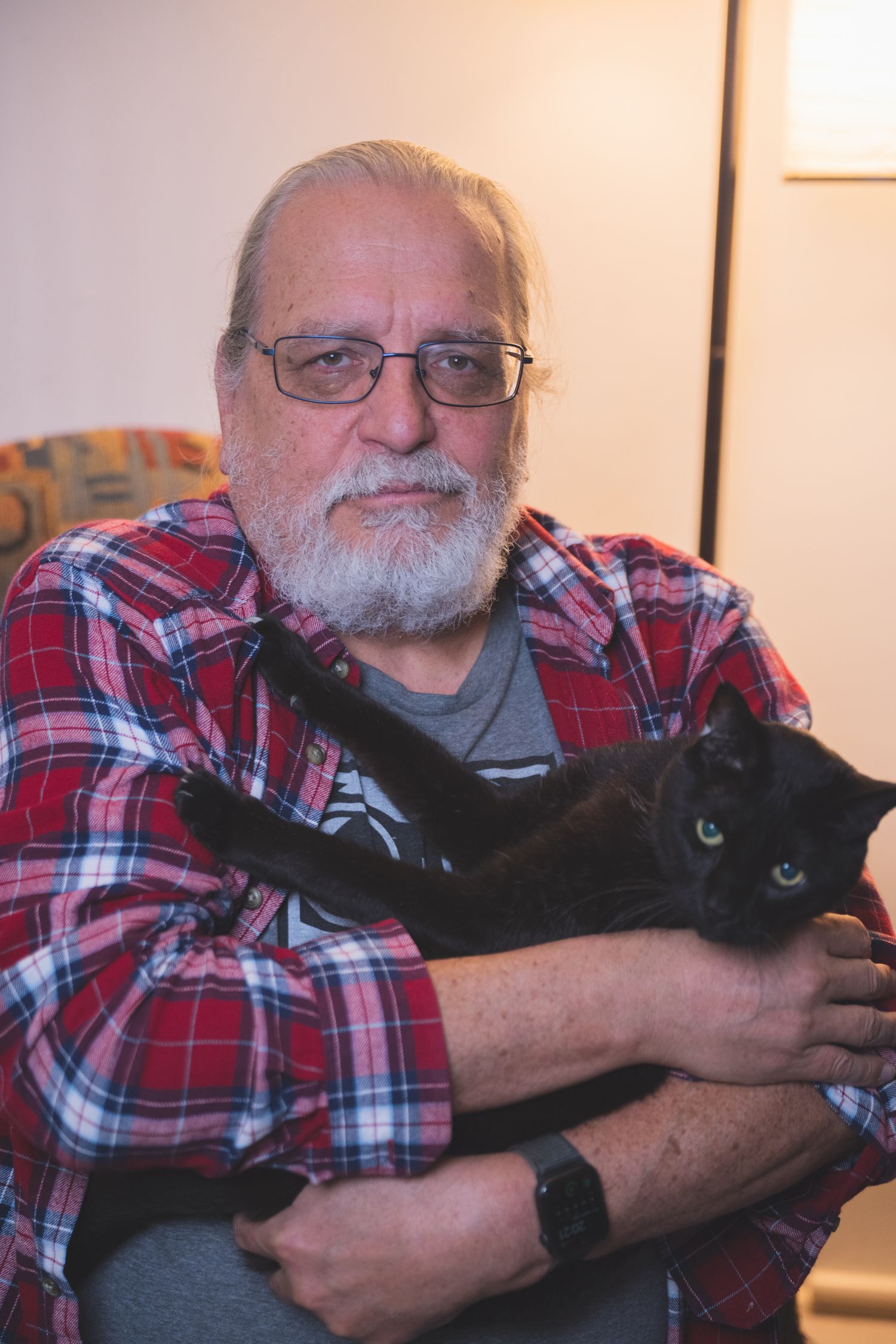 Person in plaid shirt holding black cat while relaxing on couch.