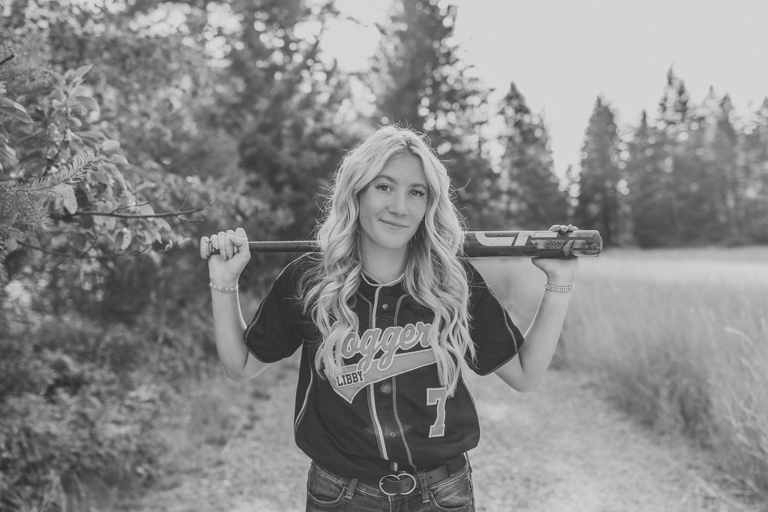 A person in a baseball jersey poses with a bat on a scenic mountain trail.