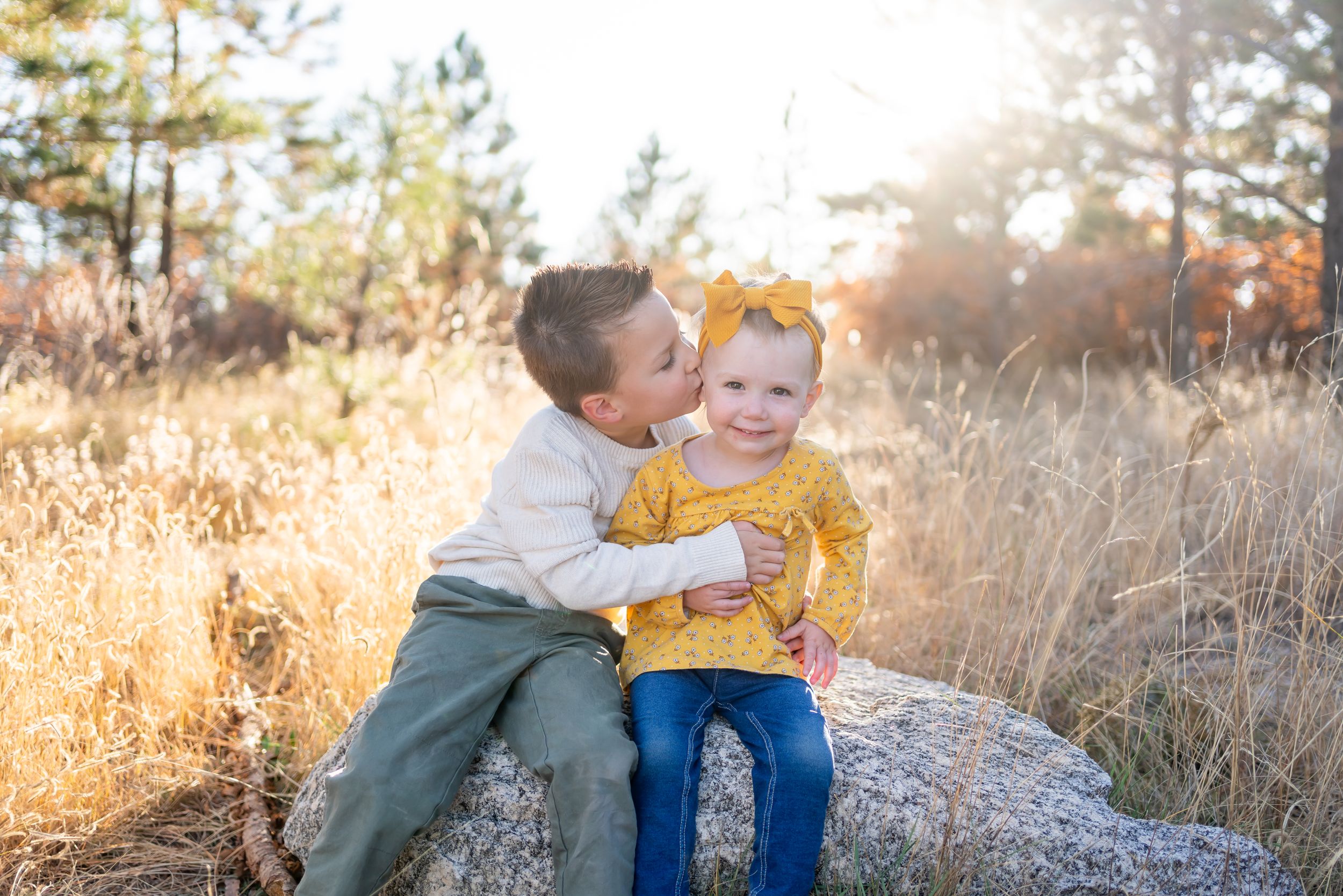 Two children sharing tender moment while sitting on rock in golden autumn field.
