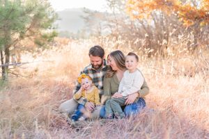 Family of four cuddling together in autumn field with warm sunset lighting.