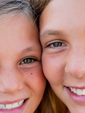 Close-up portrait of two children's faces showing bright smiles and green eyes.