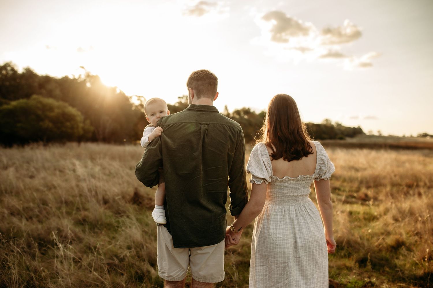 A family walks into the sunset with their son looking over their shoulder at the camera.