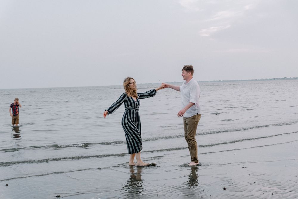 Two people hold hands while balancing on wet beach sand near ocean.