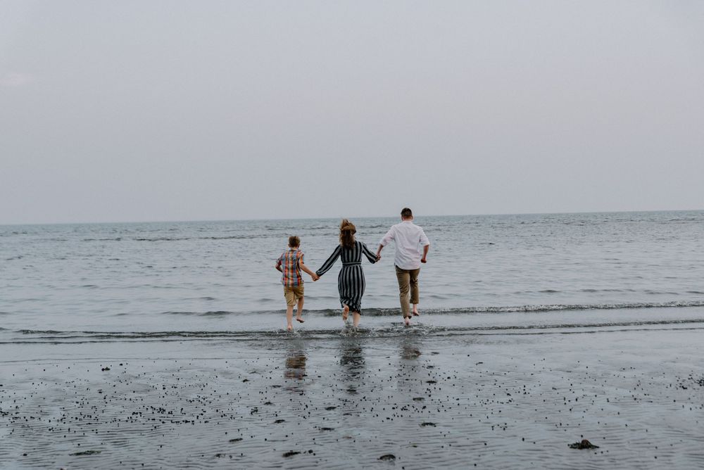 Three figures walk hand in hand along a misty beach shoreline.