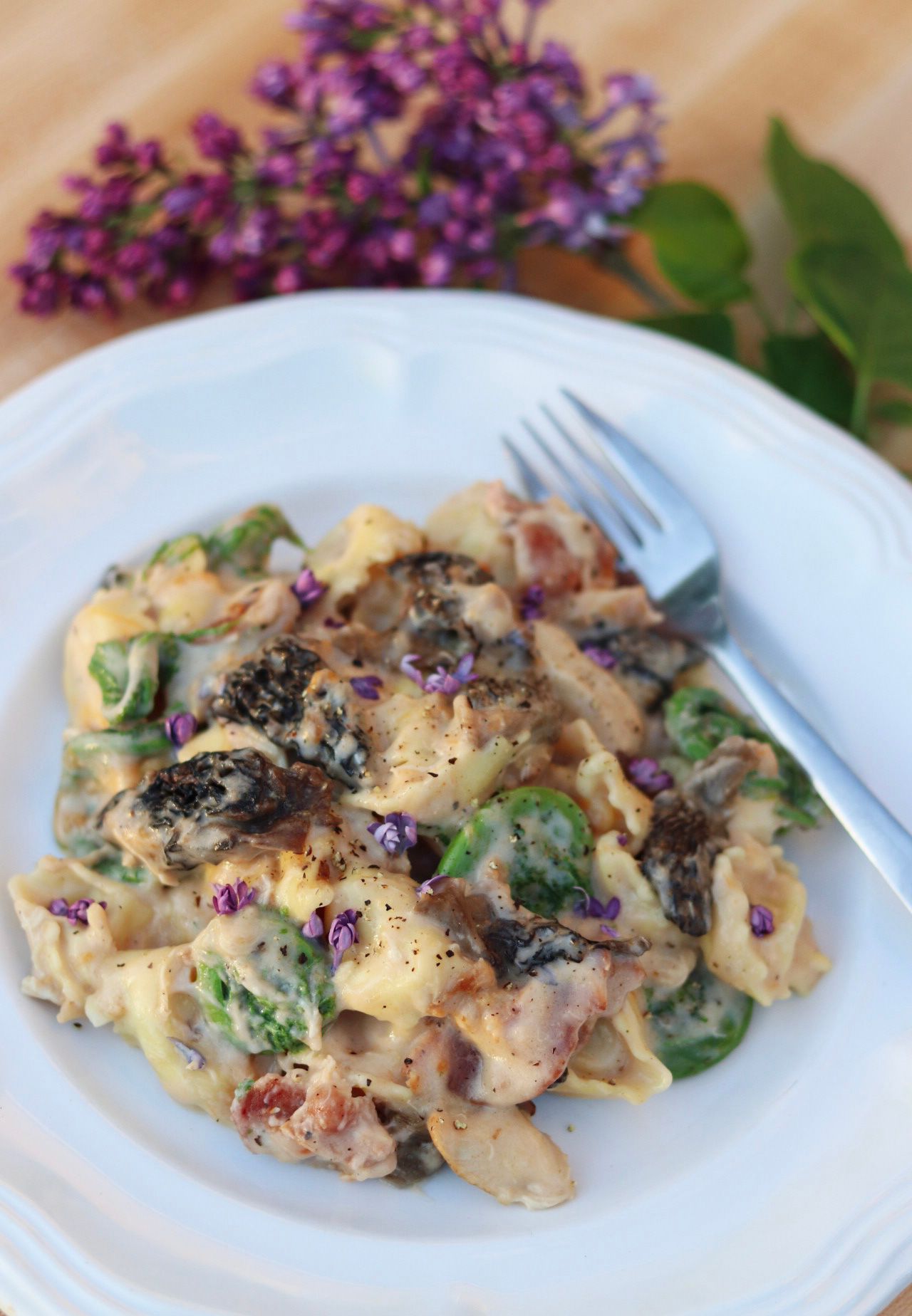 Close-up of creamy pasta with mushrooms and purple flowers as garnish.