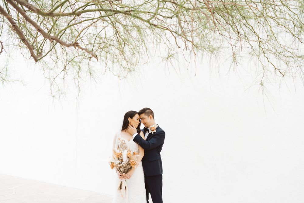 Intimate black and white portrait of couple with dried flower bouquet against white wall.
