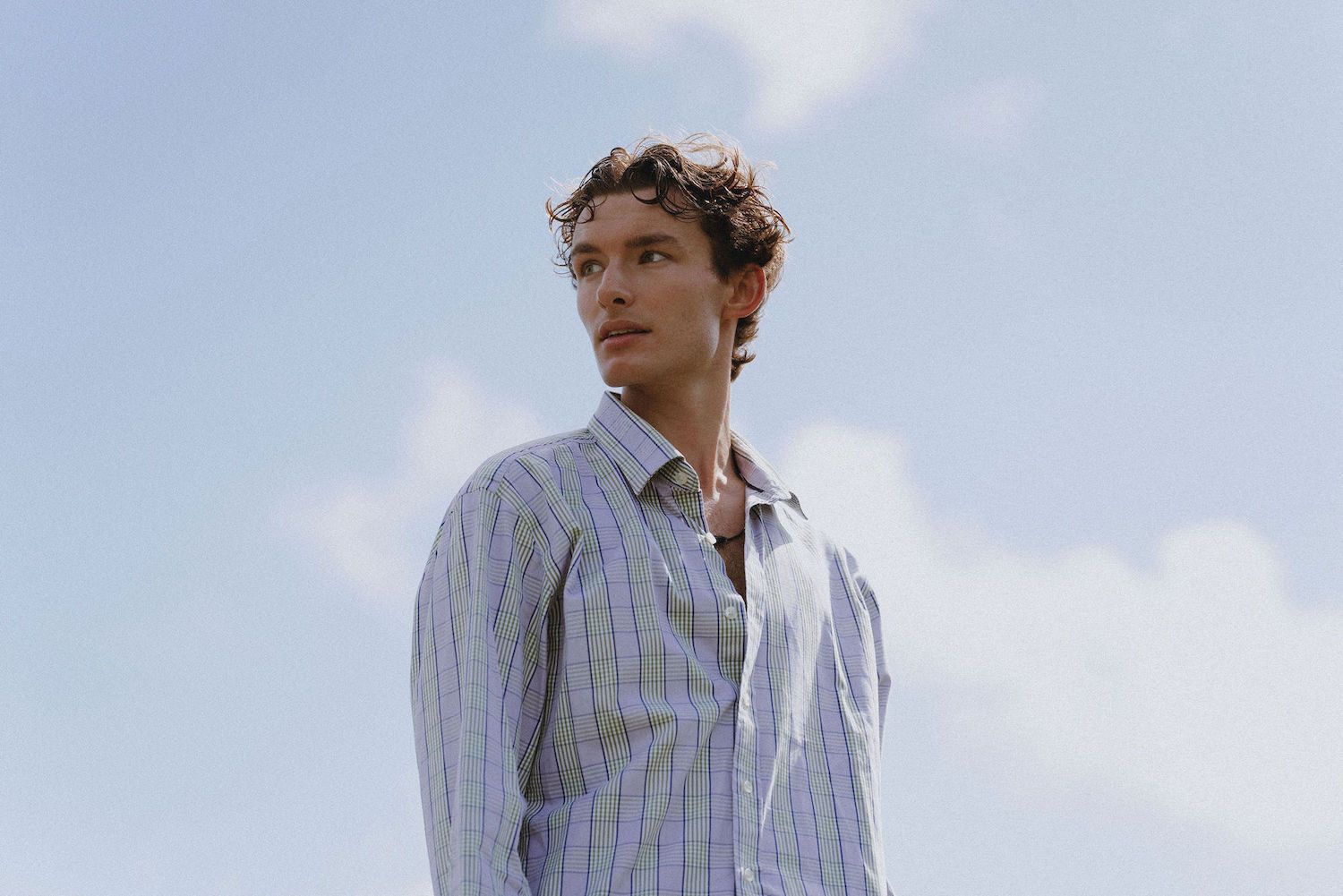 An upward angle portrait showing someone in a striped shirt against a cloudy blue sky.
