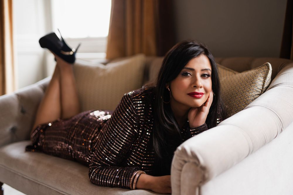 Woman in sequined dress lounges on beige couch in glamorous pose in Guildford, Surrey.