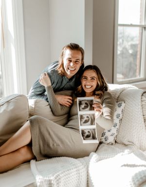 Couple on couch sharing joyful moment while holding ultrasound photos.