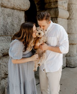 Couple in coordinated outfits sharing tender moment with small fluffy dog.
