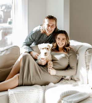 A cozy family portrait on white couch with small white dog.