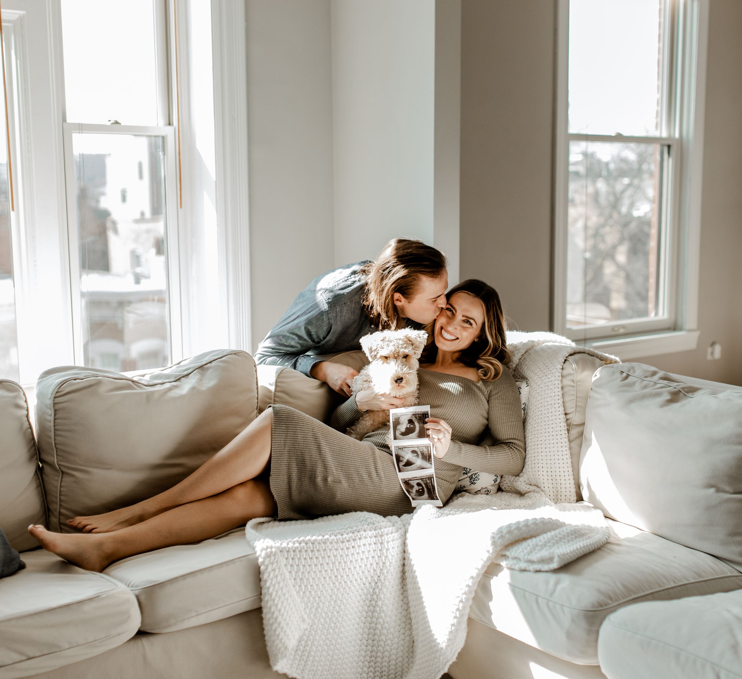 Couple snuggling on a cozy gray couch by window with coffee and affection.