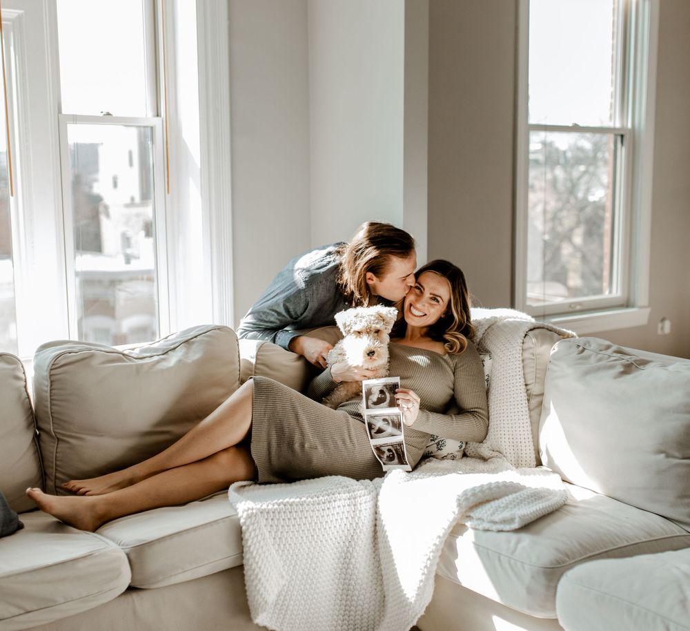 Couple snuggling on a cozy gray couch by window with coffee and affection.