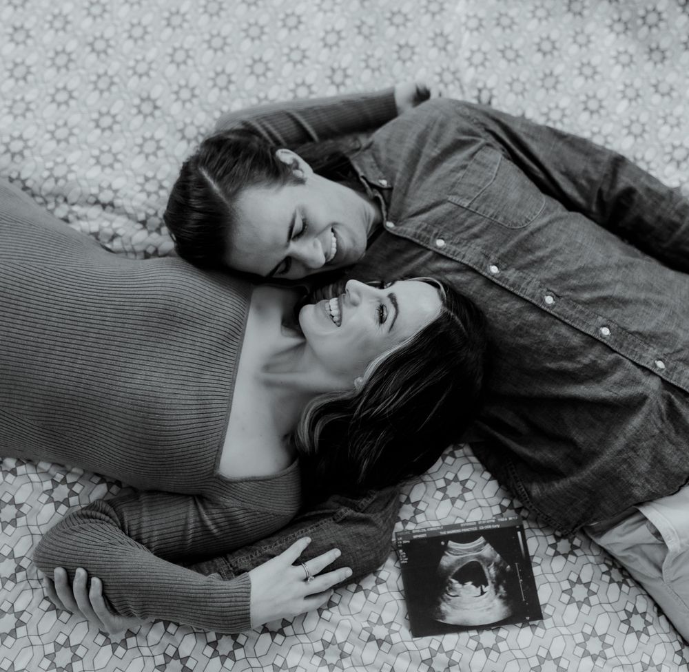 A black and white pregnancy announcement photo with ultrasound image on patterned bedding.