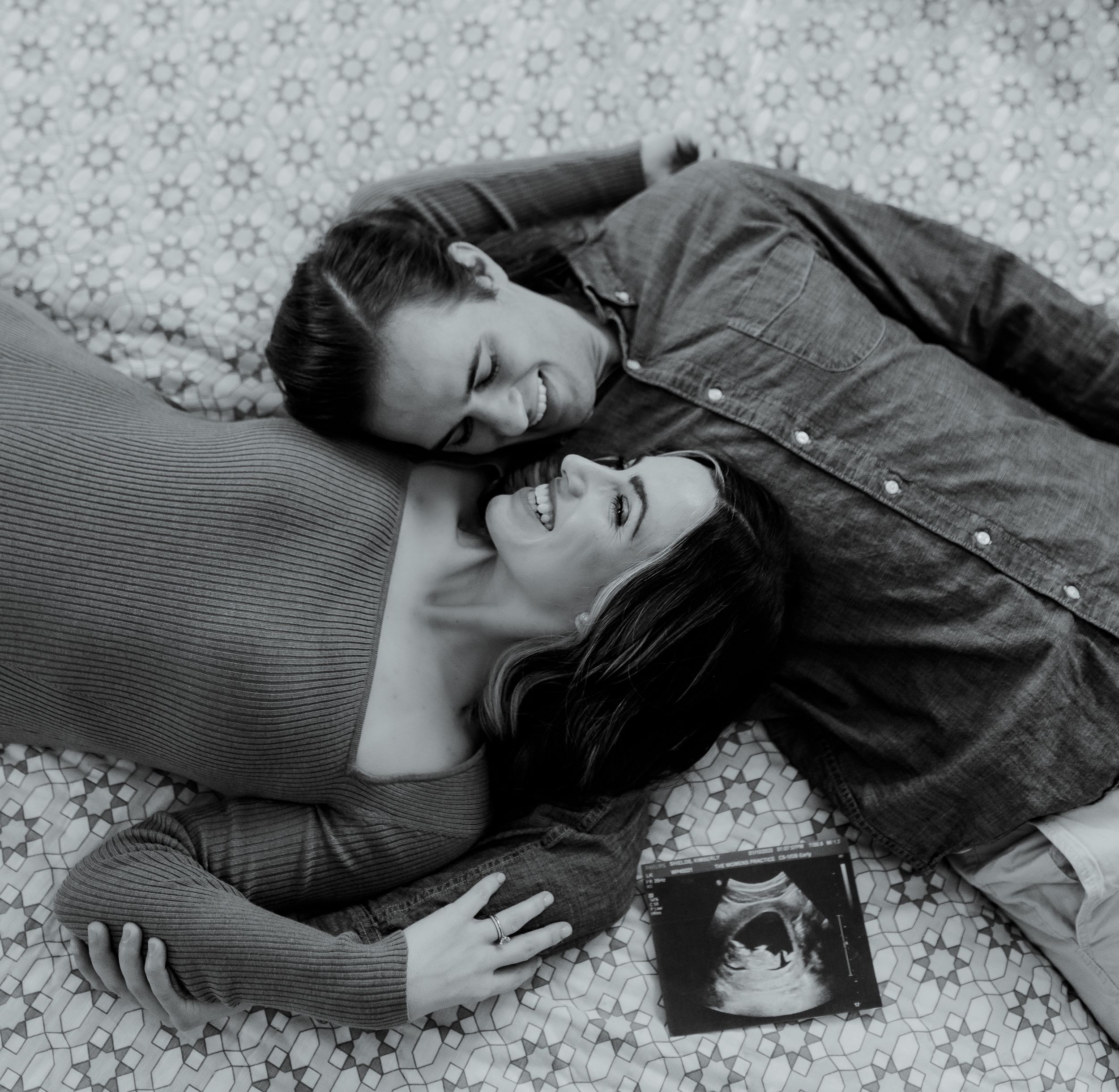 A black and white pregnancy announcement photo with ultrasound image on patterned bedding.