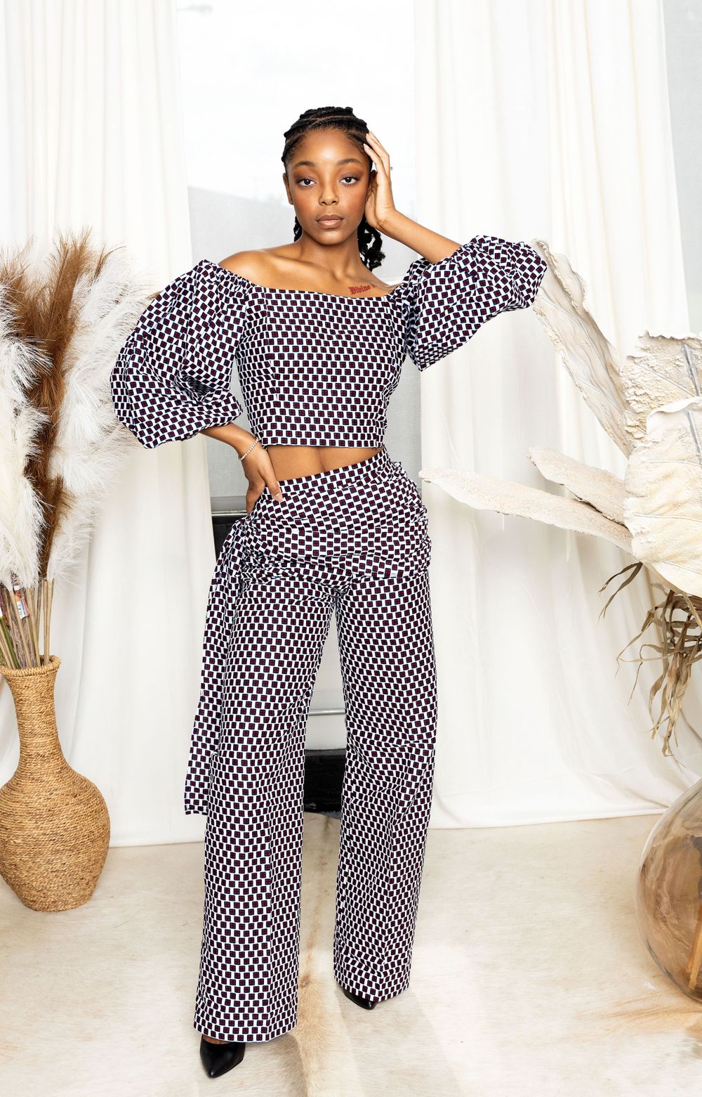Model wearing navy polka dot two-piece outfit posing against white backdrop with decorative elements.