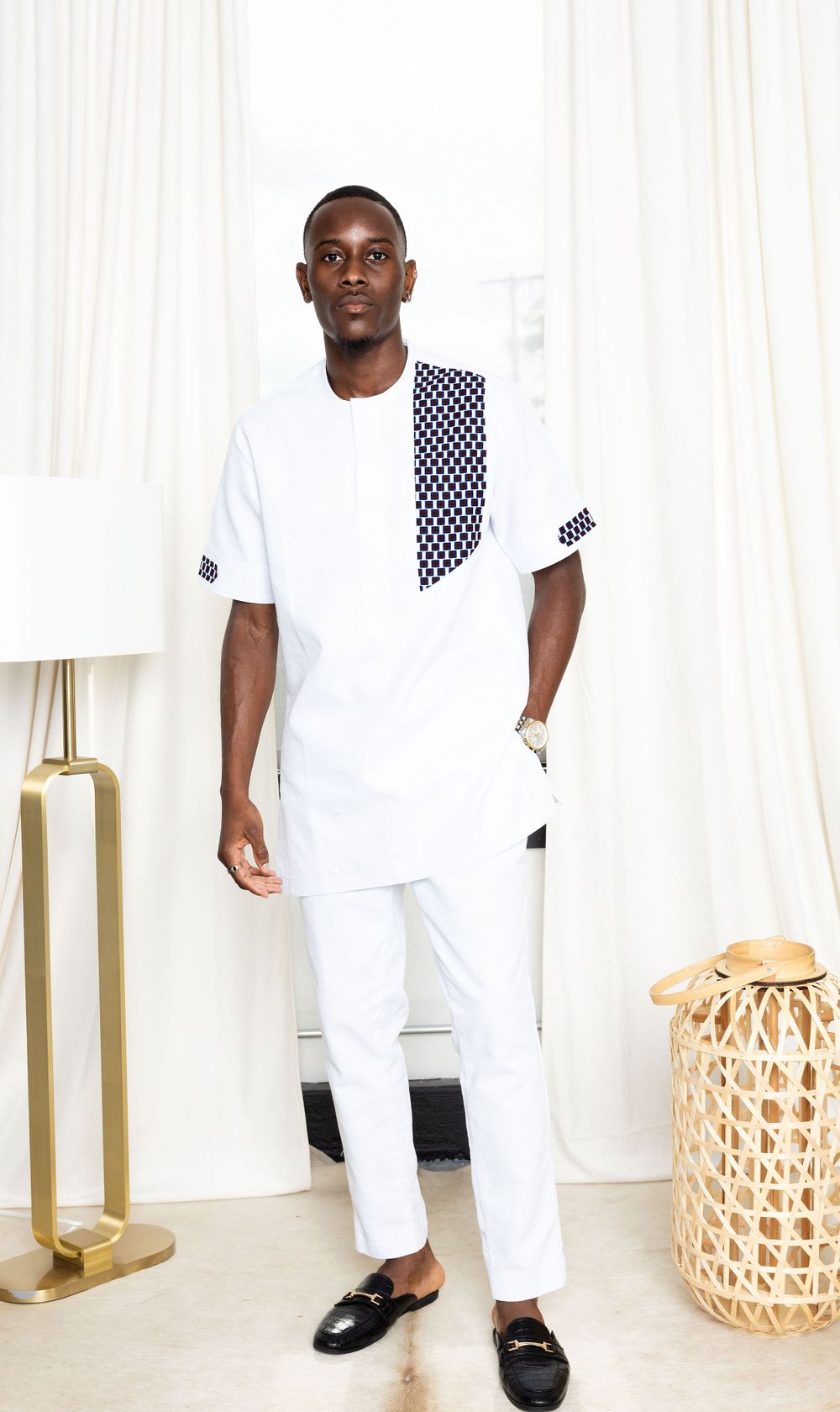 Person wearing all-white outfit with black accents posing in modern interior setting.