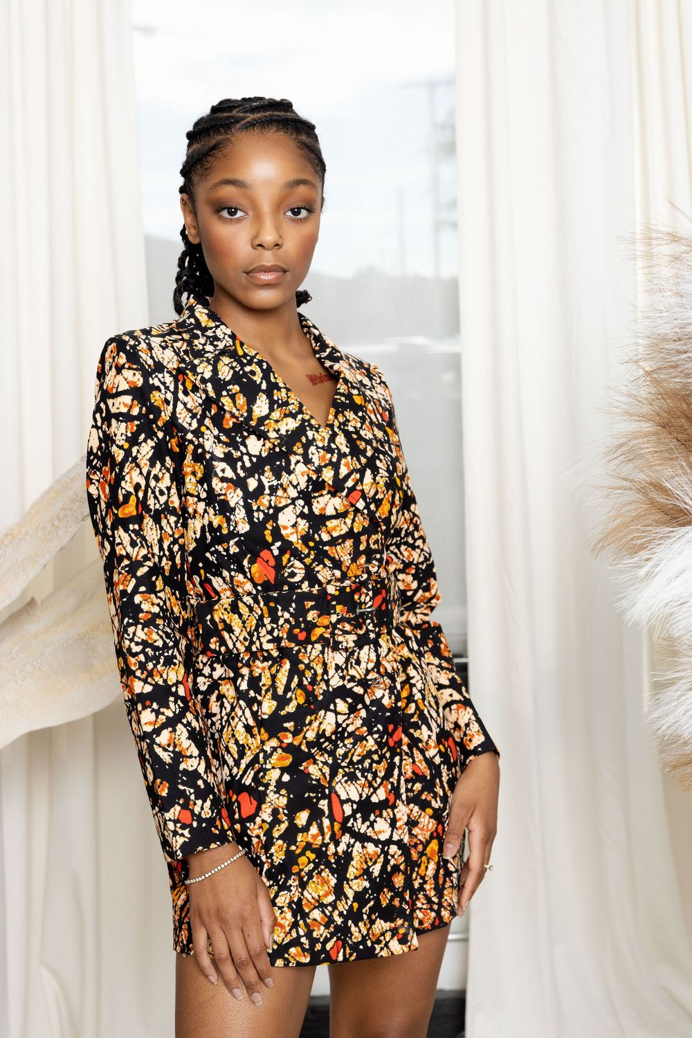 Model wearing floral print dress poses elegantly against white curtain backdrop.