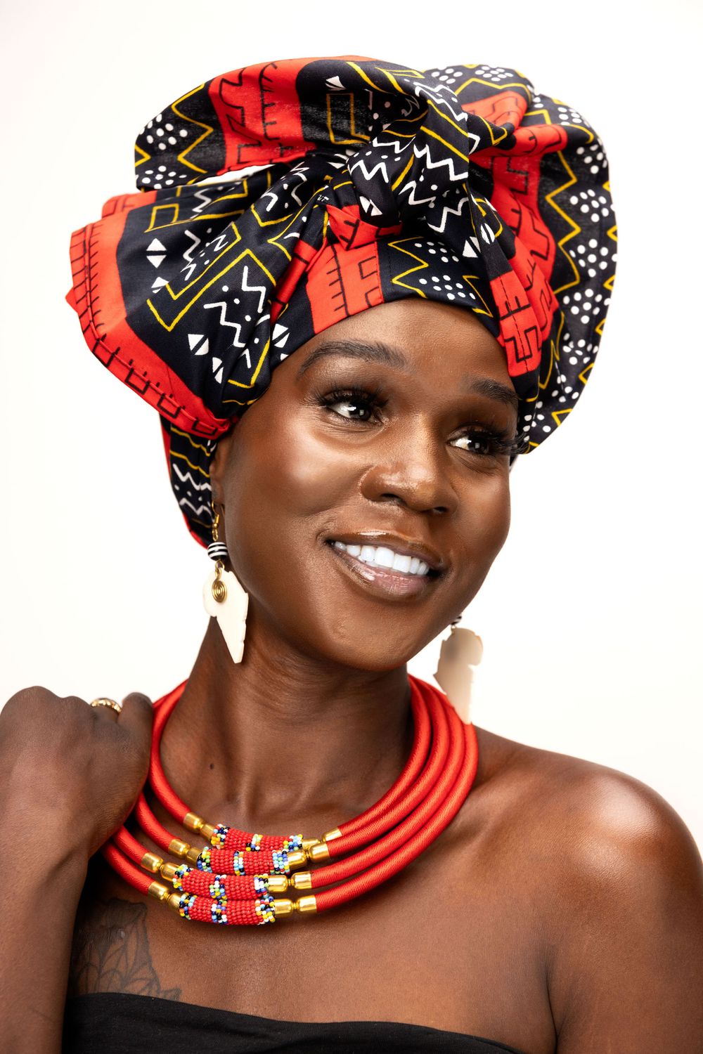 Person wearing red and black patterned headwrap with matching beaded necklace poses elegantly.