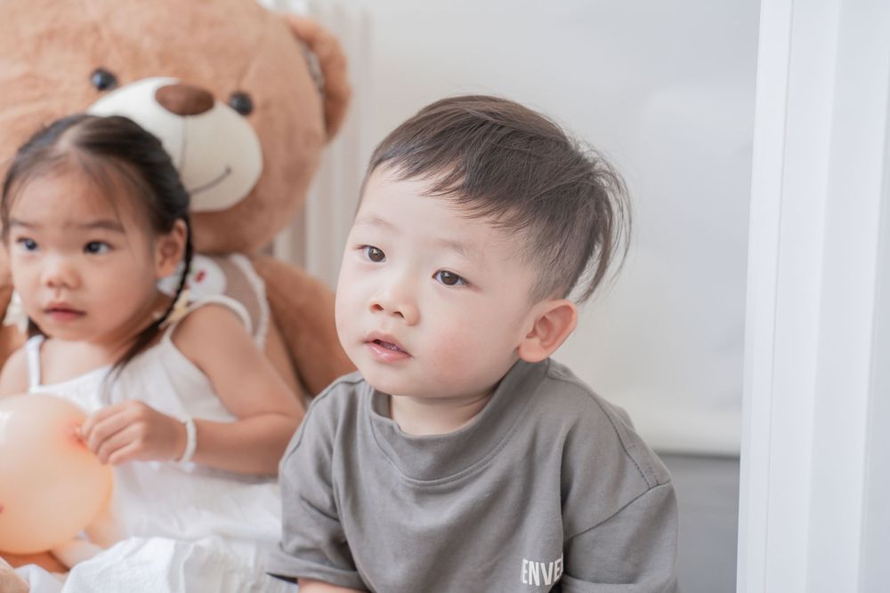 Children sitting indoors with a large teddy bear in soft lighting.