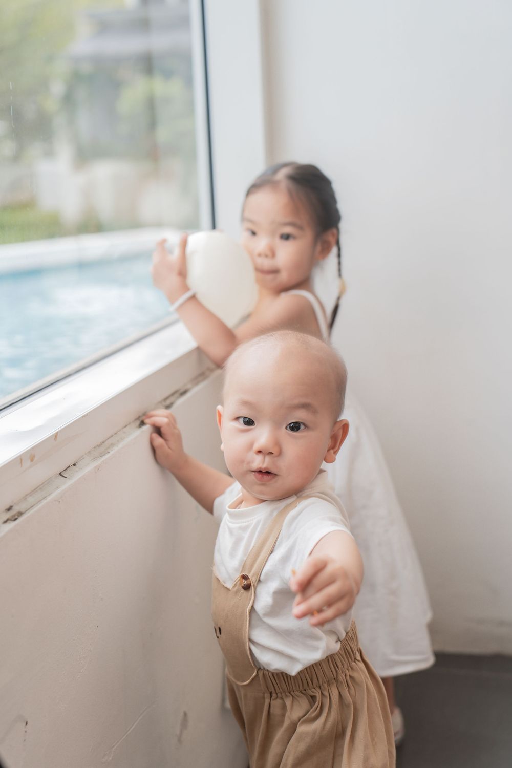 Children look out a window together while standing in a bright indoor space.