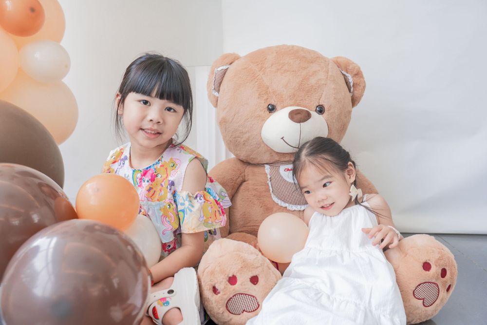 Children posing with large teddy bears and balloons in studio setting.