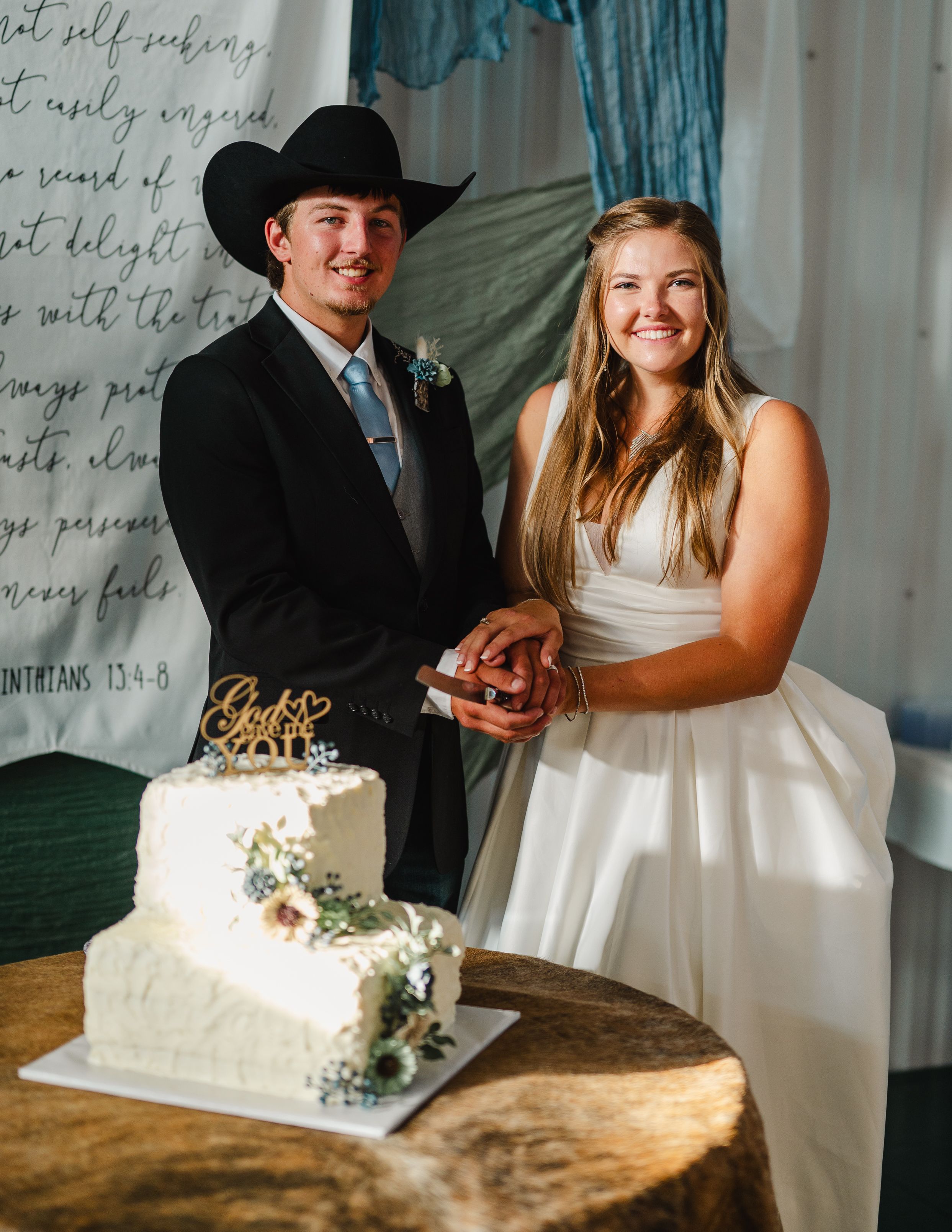 A wedding couple in western attire cutting their elegant white wedding cake together.