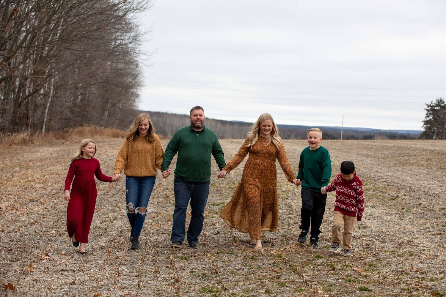 A family walking together holding hands across a winter field landscape.