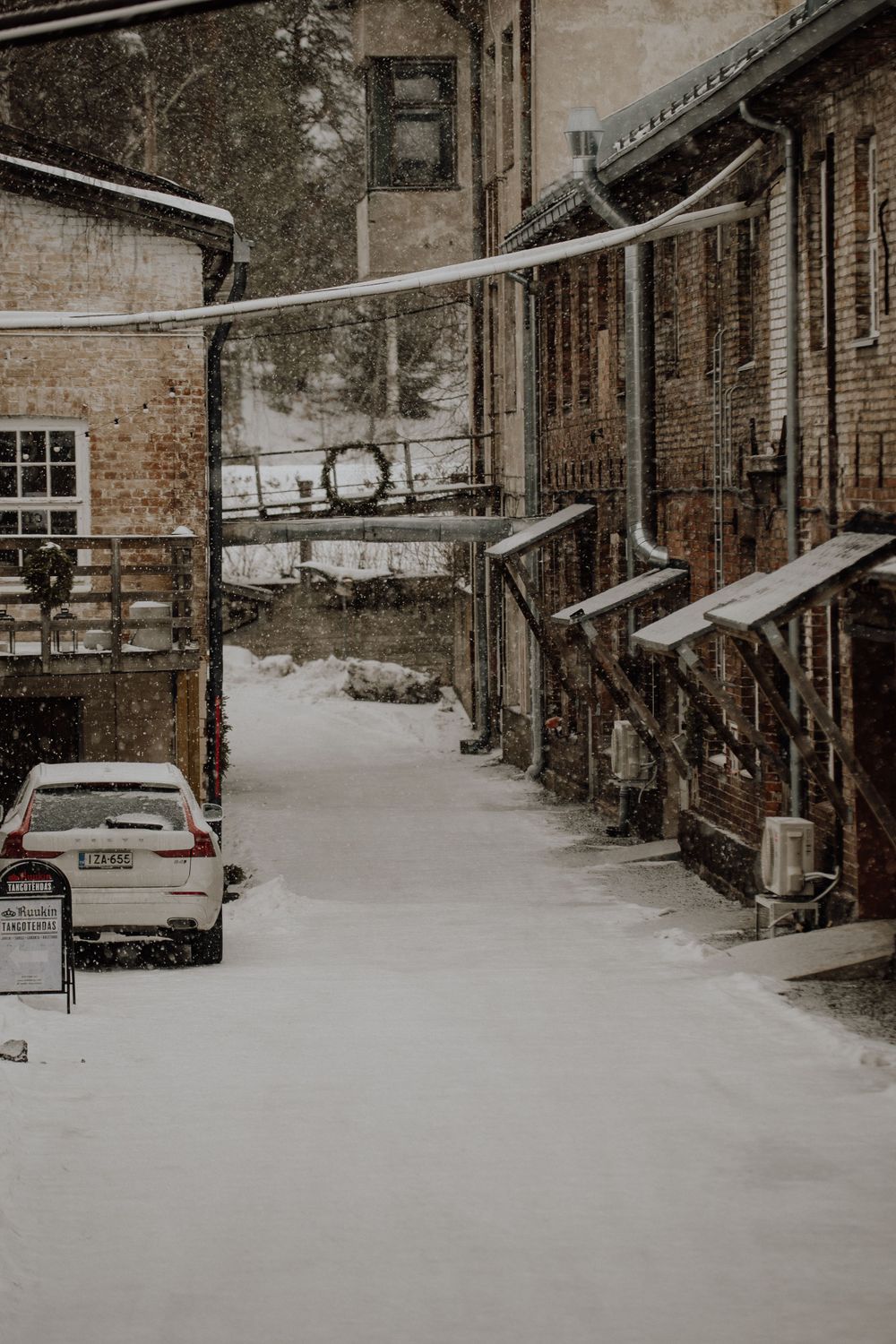 Snow covered alley between brick buildings with a parked car.