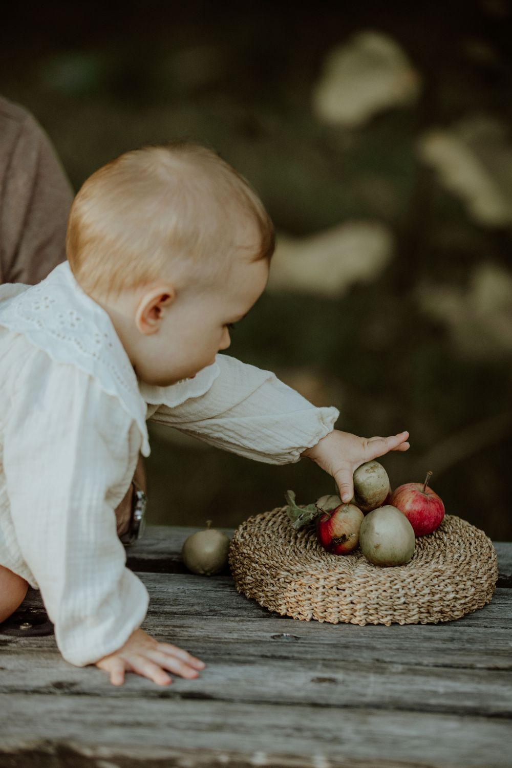 Young child reaching for apples and pears on woven mat.