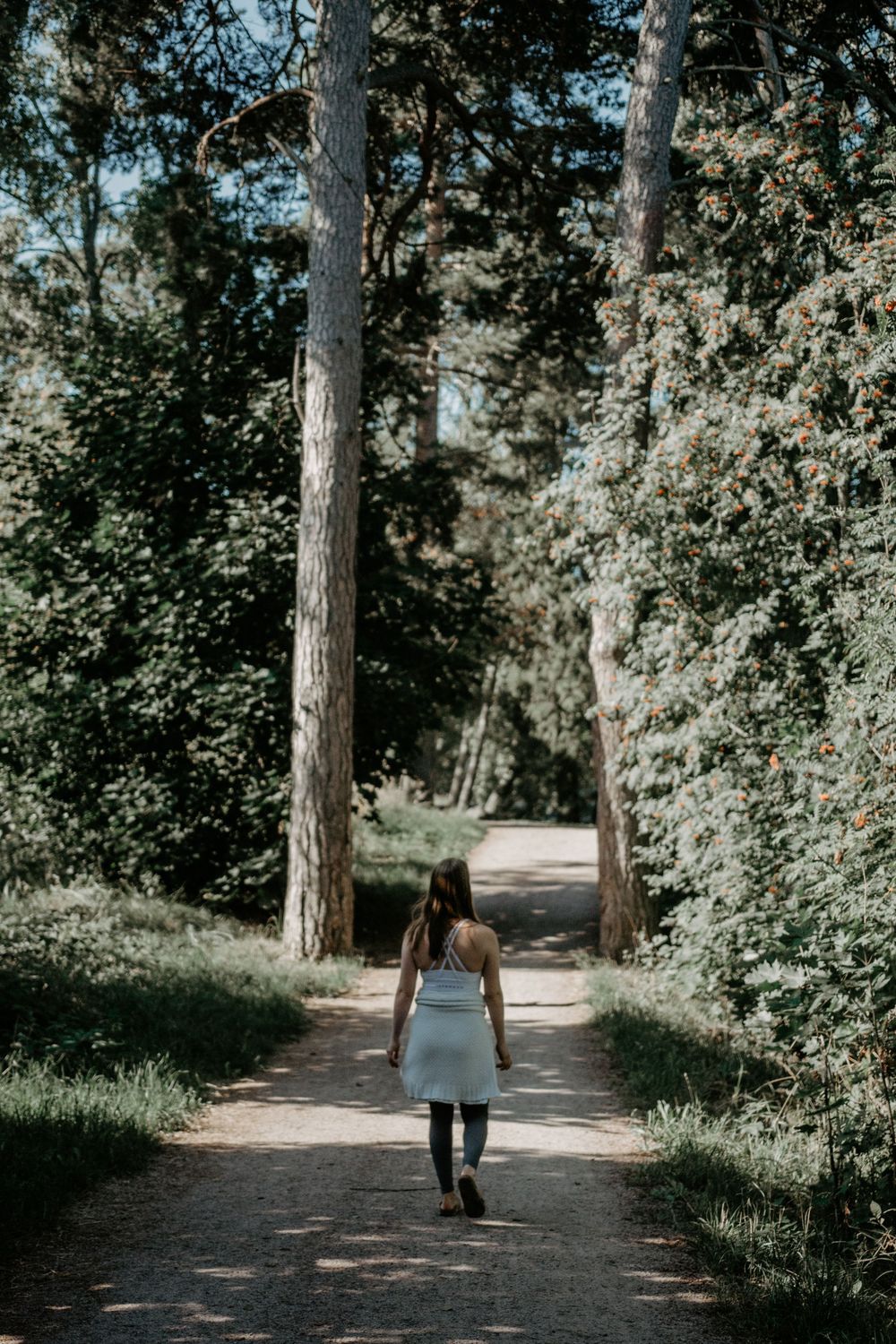 Person in dress walking alone on tree-lined forest path.