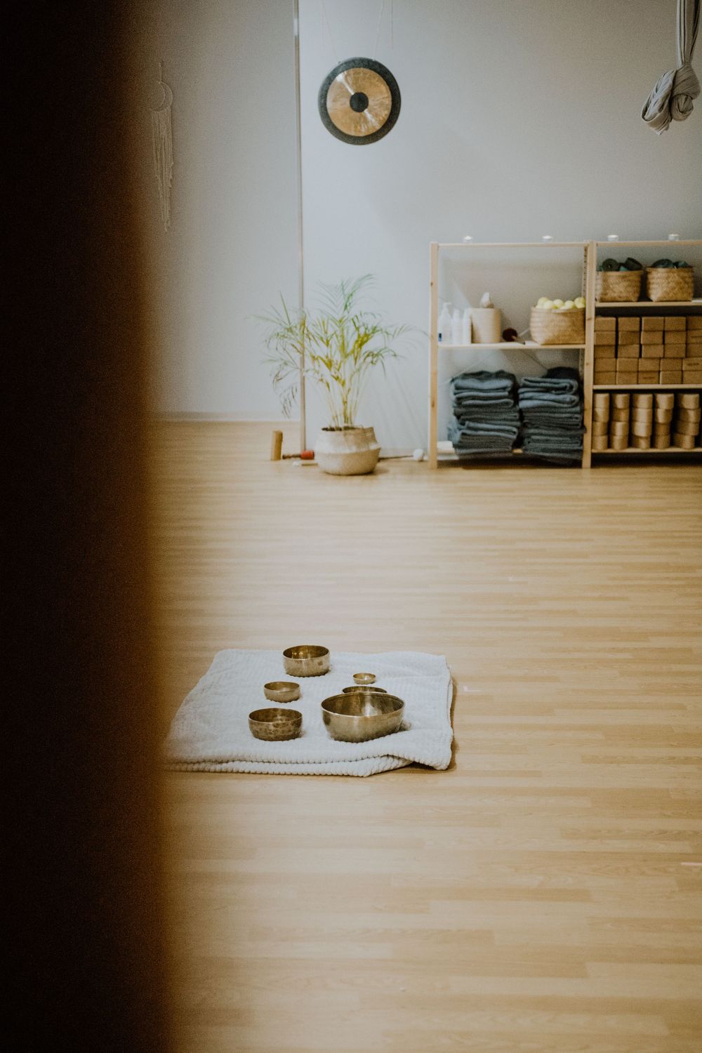 Minimalist spa room with wooden shelves, folded towels and singing bowls on floor.
