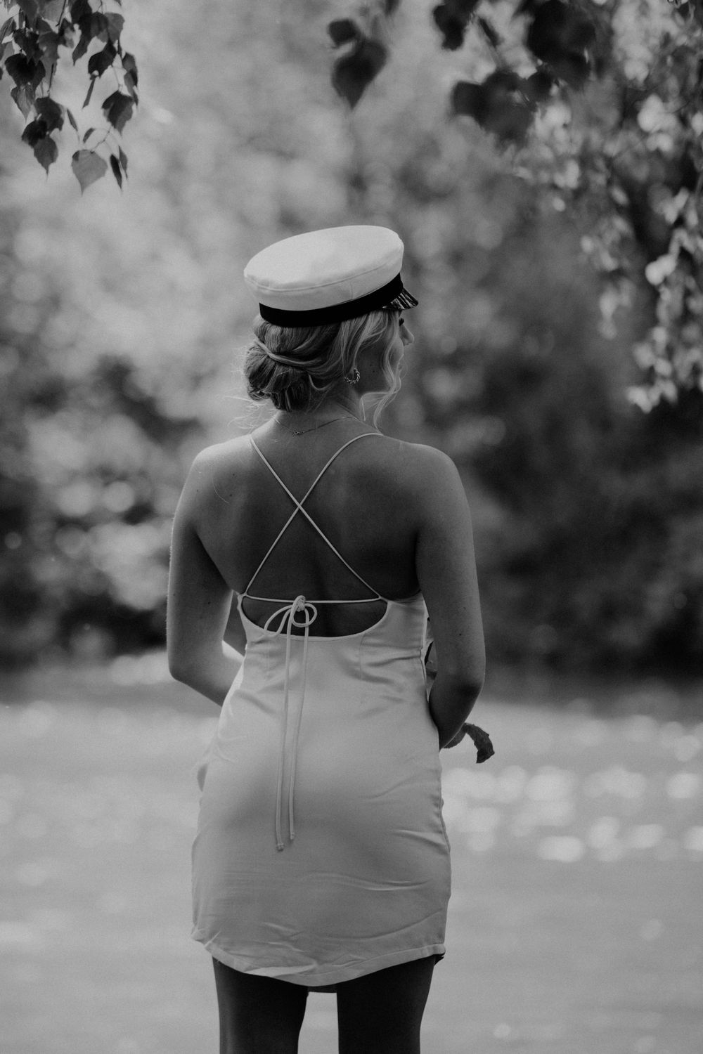 Back view of person in white dress and cap standing in garden.