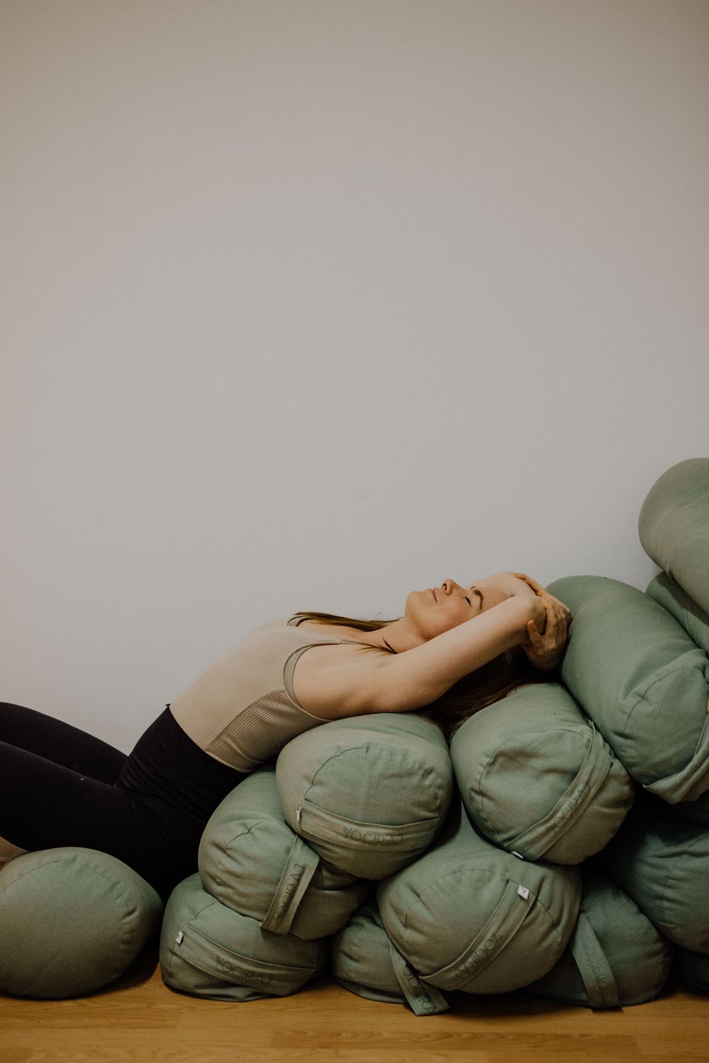 Person resting on pile of sage green cushions against white wall.
