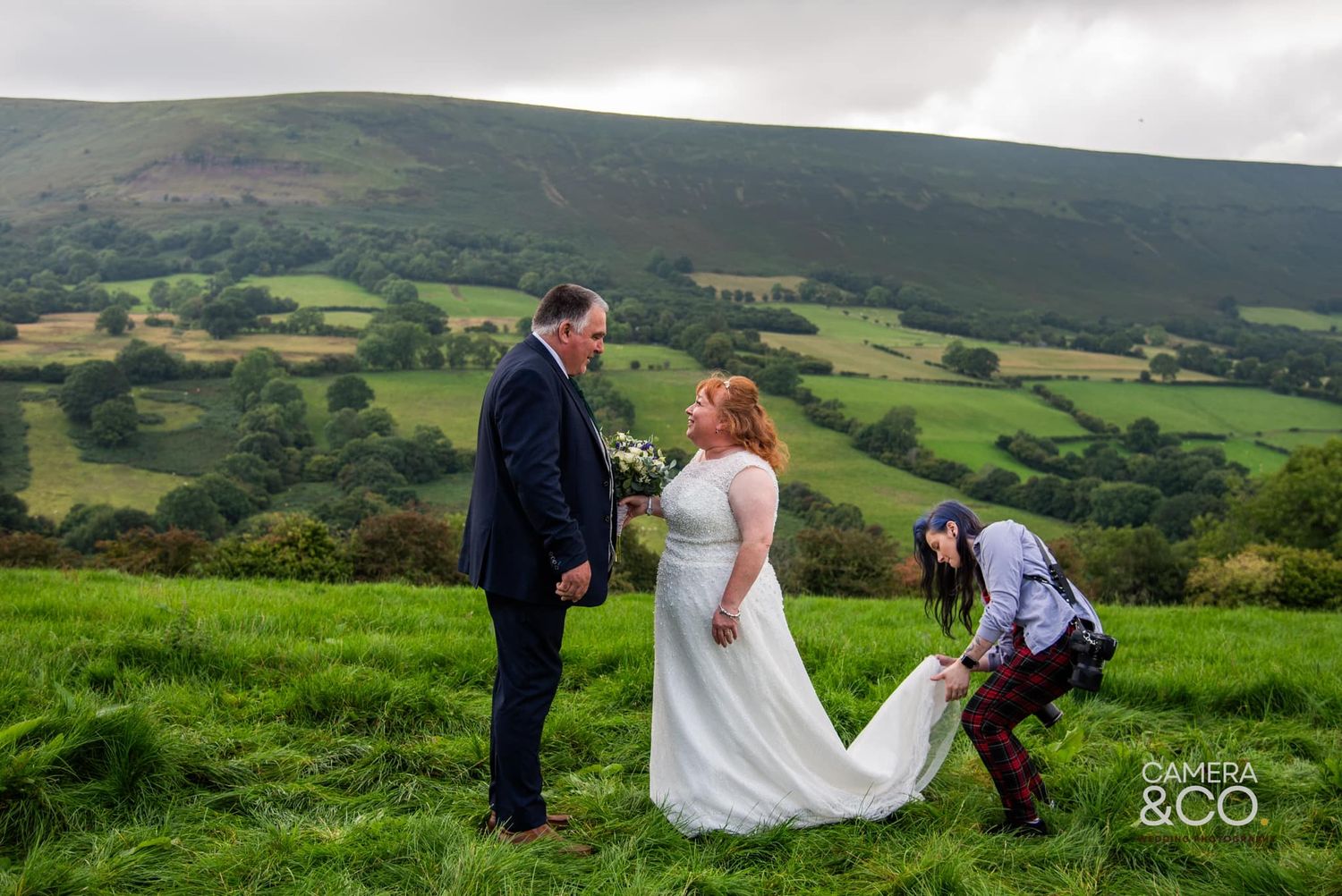 A wedding couple photographed against rolling green hills and countryside.