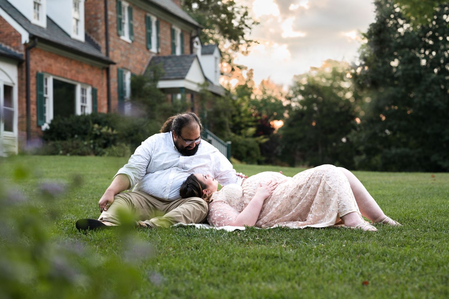 Couple relaxing together on grass during sunset near brick house.