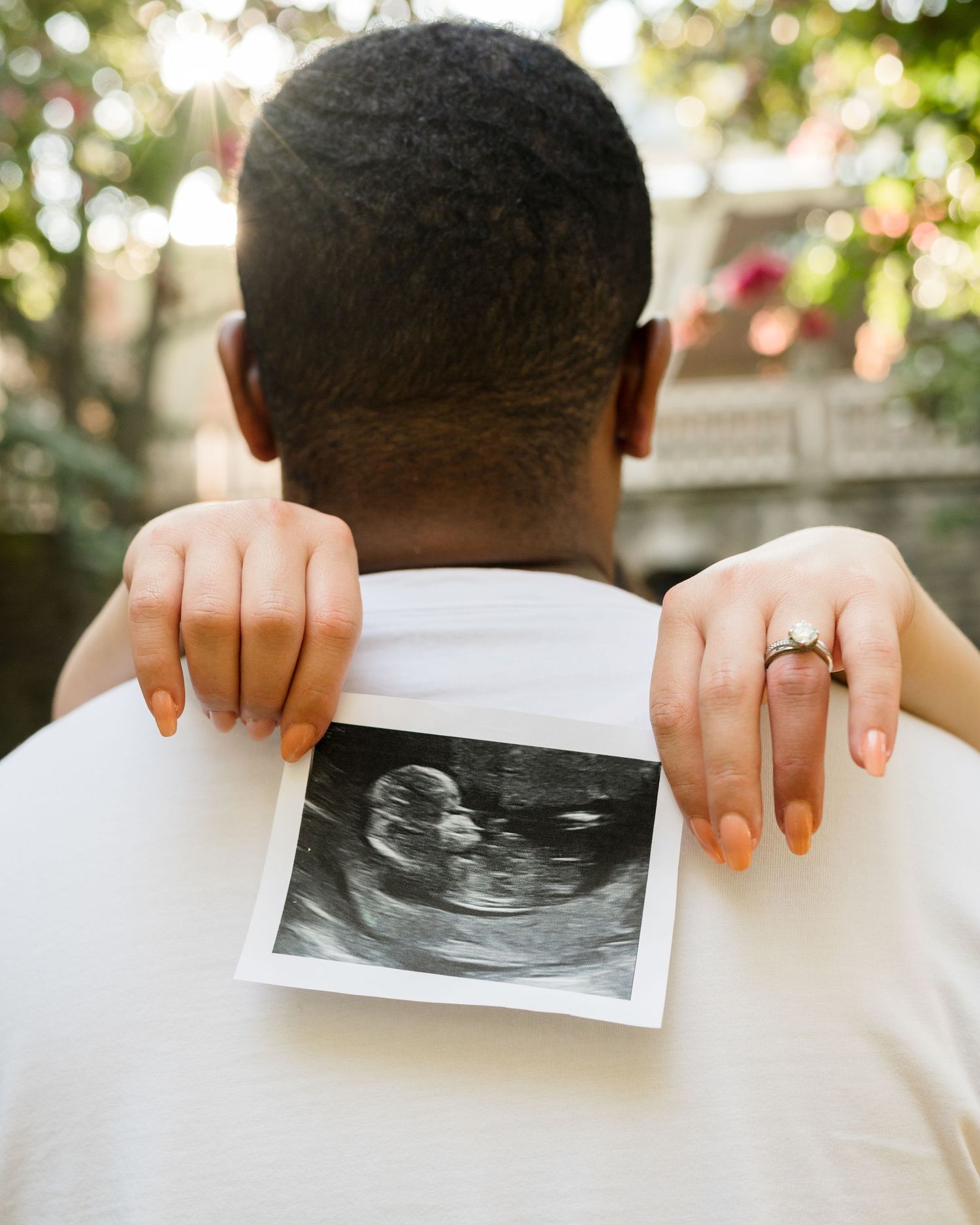 Person holding ultrasound photo against white shirt revealing pregnancy announcement.