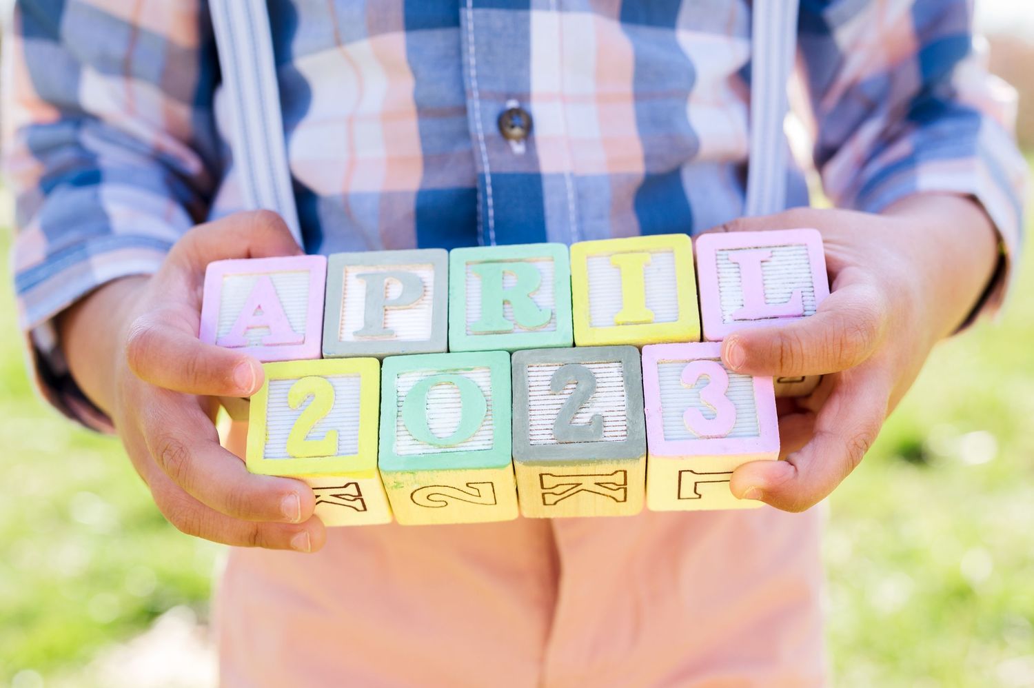 Hands holding pastel colored baby blocks spelling out a word.