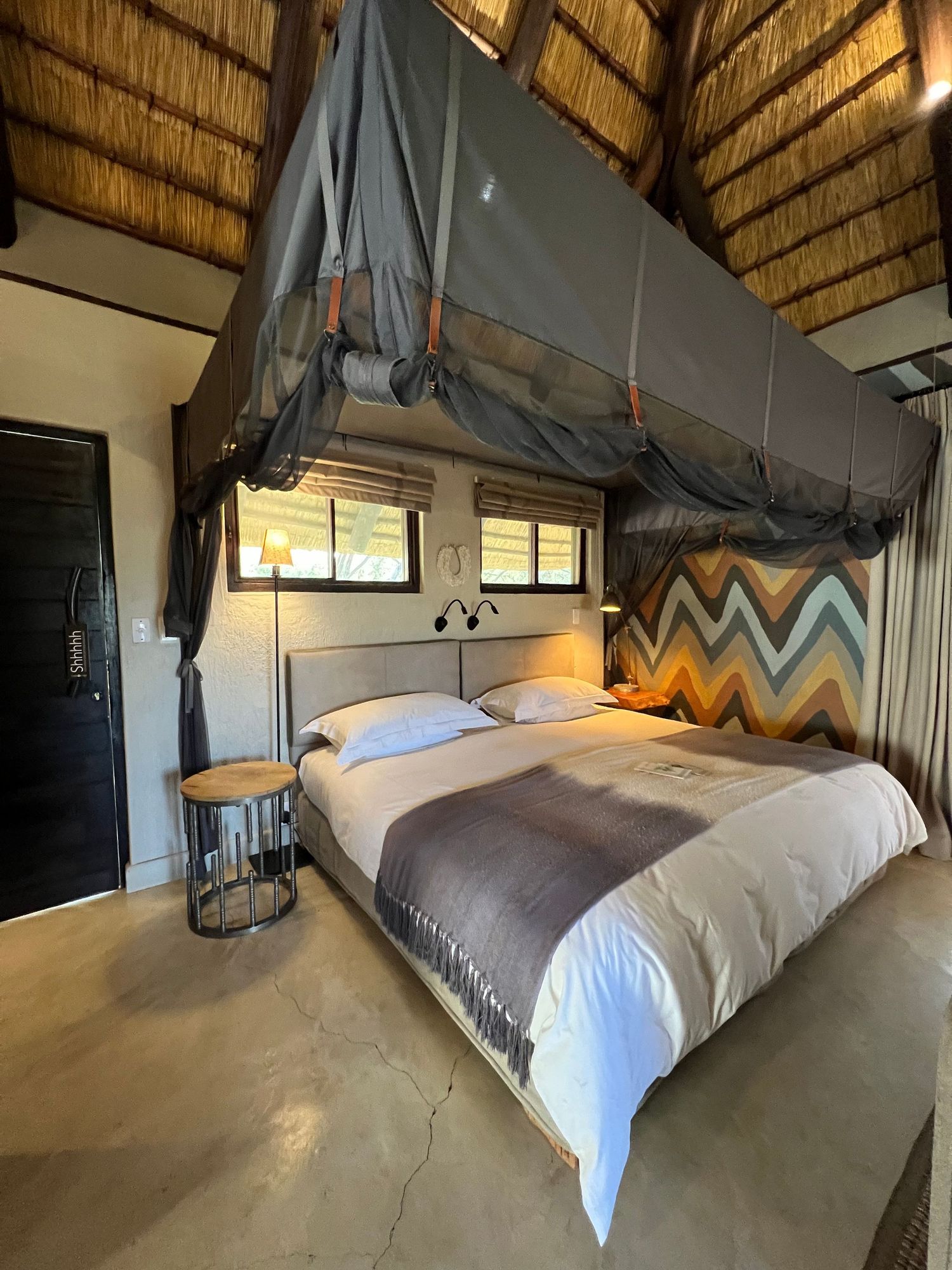 Safari lodge bedroom with thatched roof and chevron-patterned headboard in earth tones.