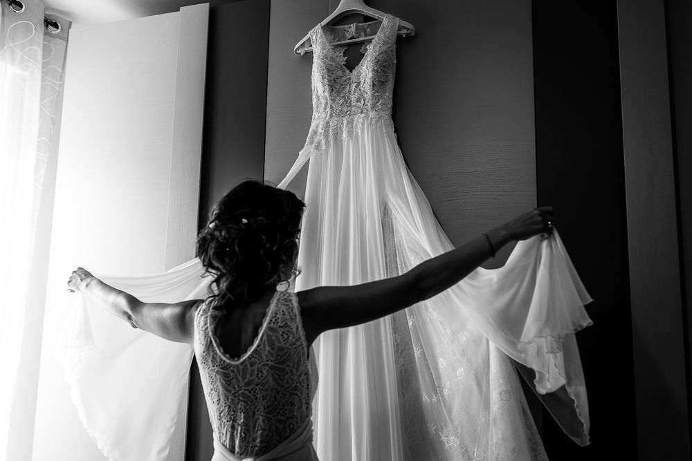 Silhouette of dress preparation with wedding gown hanging in background.