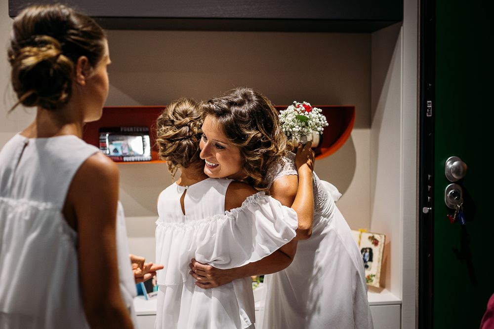 Young attendants in white dresses with hair rollers prepare in a dressing room for a wedding event.