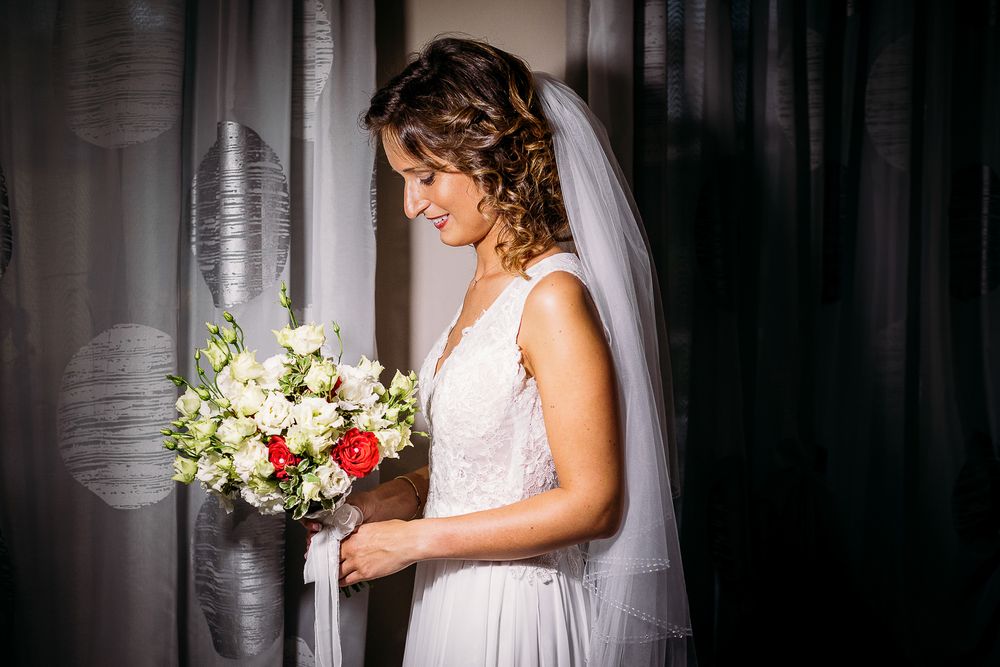 Elegant bride in lace dress holds a beautiful bouquet of white and pink flowers.