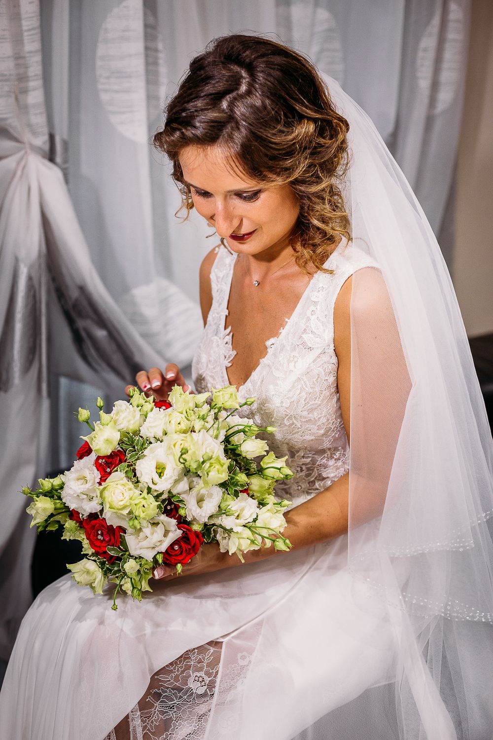 Bride in white lace gown gazes down at her colorful wedding bouquet.