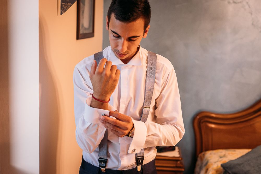 Groom adjusts his cufflinks while getting ready in formal attire with suspenders.