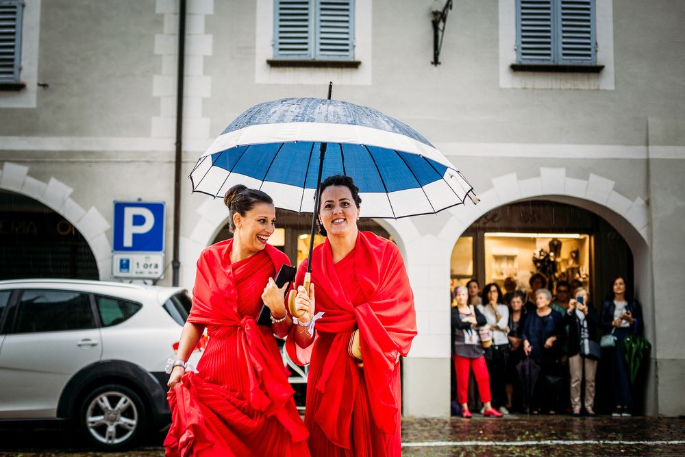 Two people in bright red attire share a white umbrella while walking together on a rainy day.