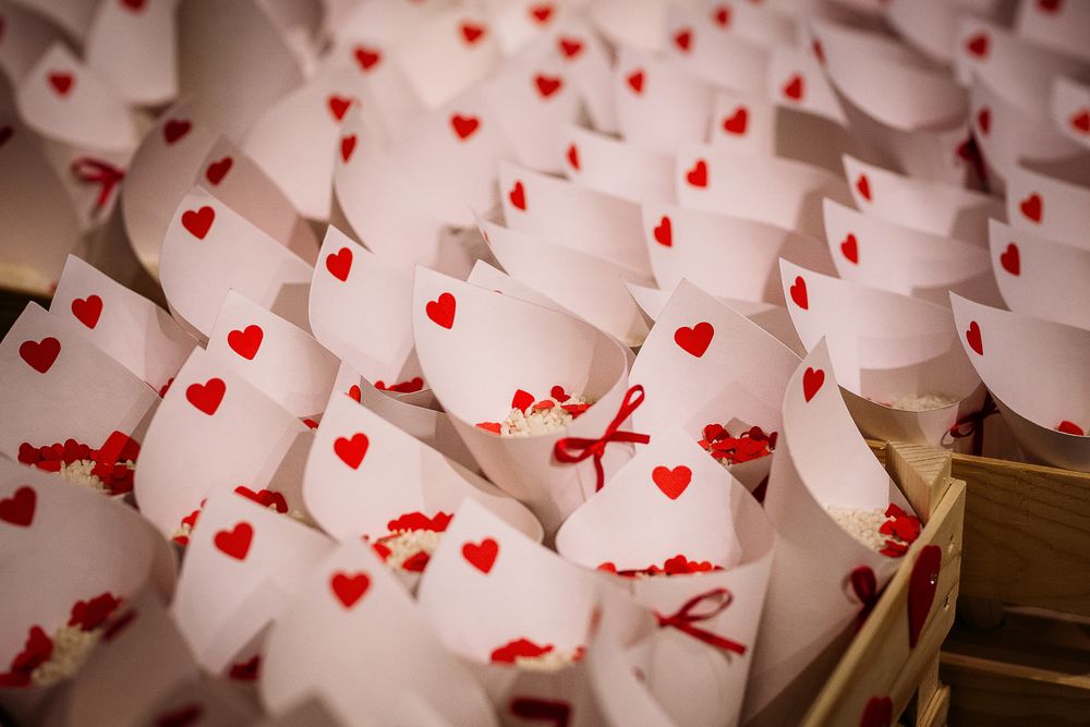 Wedding decorations featuring white paper cones with red heart patterns and ribbons.