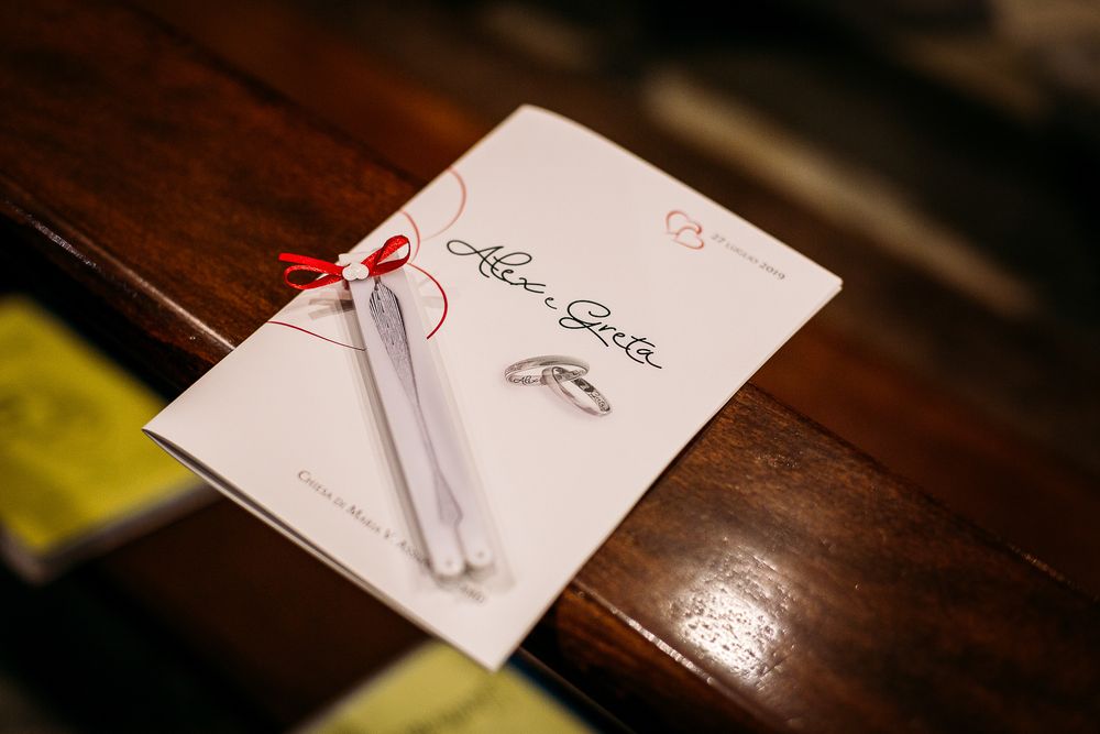 Wedding rings placed on a white paper with red ribbon on wooden surface.