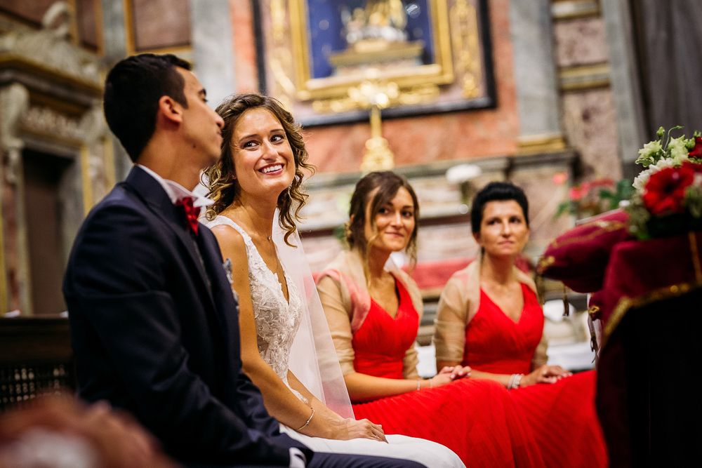 Wedding ceremony in progress inside an ornate church with red-dressed attendants.