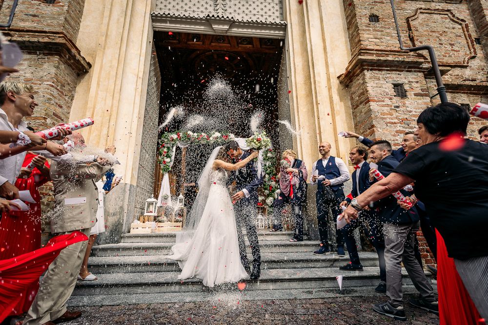 Wedding couple exits church as guests shower them with rice on stone steps.
